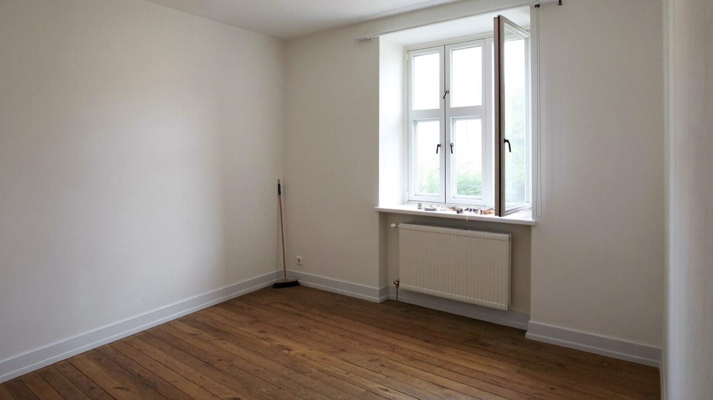 Leergeräumtes, besenreines Zimmer mit Holzdielen und Besen an der Wand nach einer Haushaltsauflösung