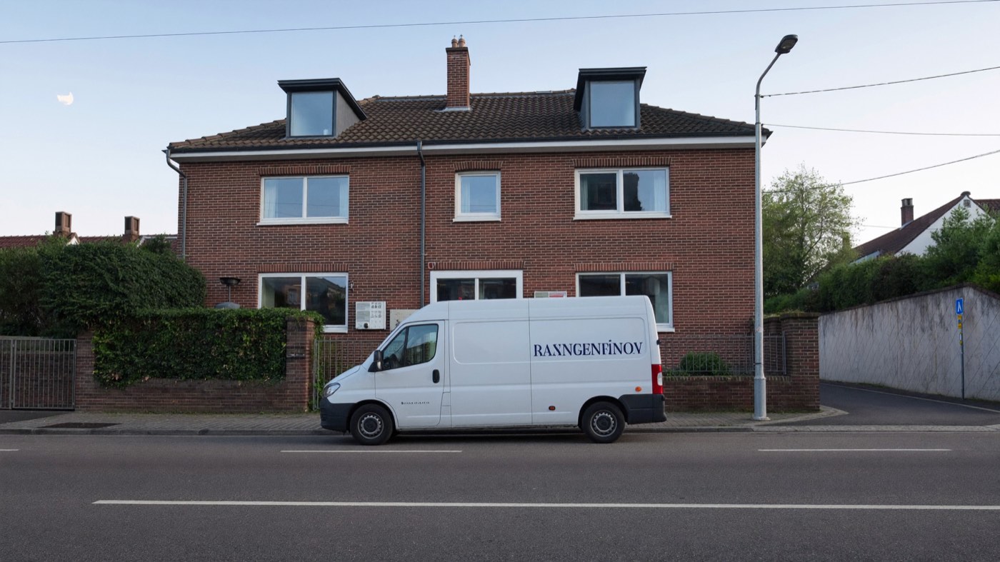 Neutraler weißer Transporter parkt in einer ruhigen Wohnstraße vor einem Mehrfamilienhaus