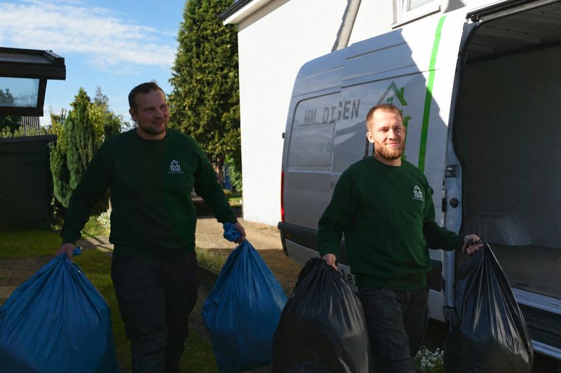 Meik Mroz und Pascal Vagts von MM Dienstleistungen tragen Müllsäcke durch einen Garten zum Transporter