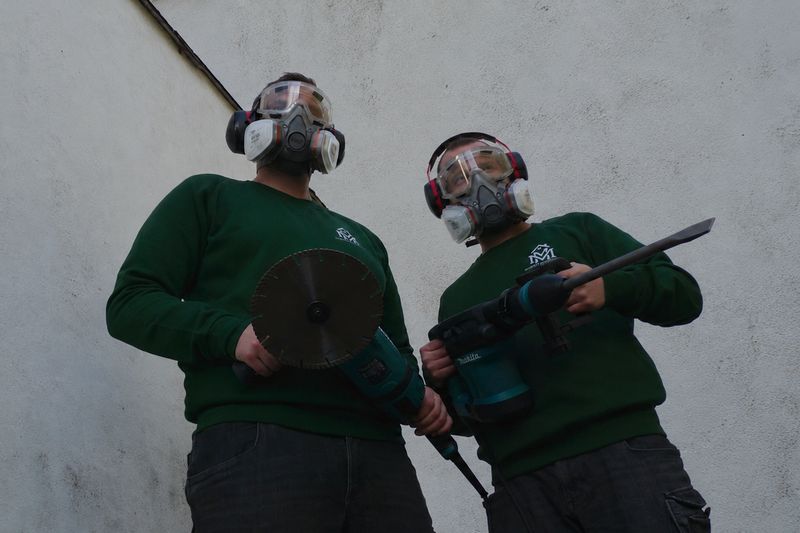 Zwei Teammitglieder von MM Dienstleistungen in Schutzausrüstung mit Trennschleifer und Stemmhammer vor einer Betonwand