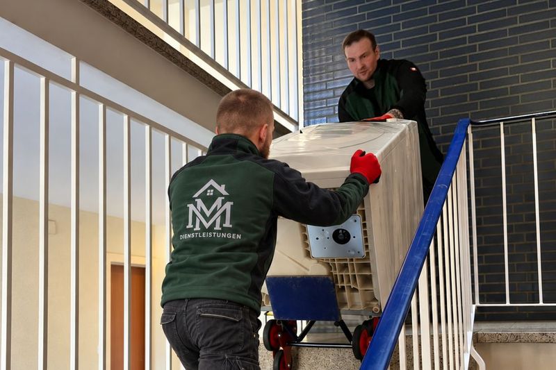Zwei Teammitglieder von MM Dienstleistungen bringen eine Waschmaschine auf einer Sackkarre die Treppe hinauf
