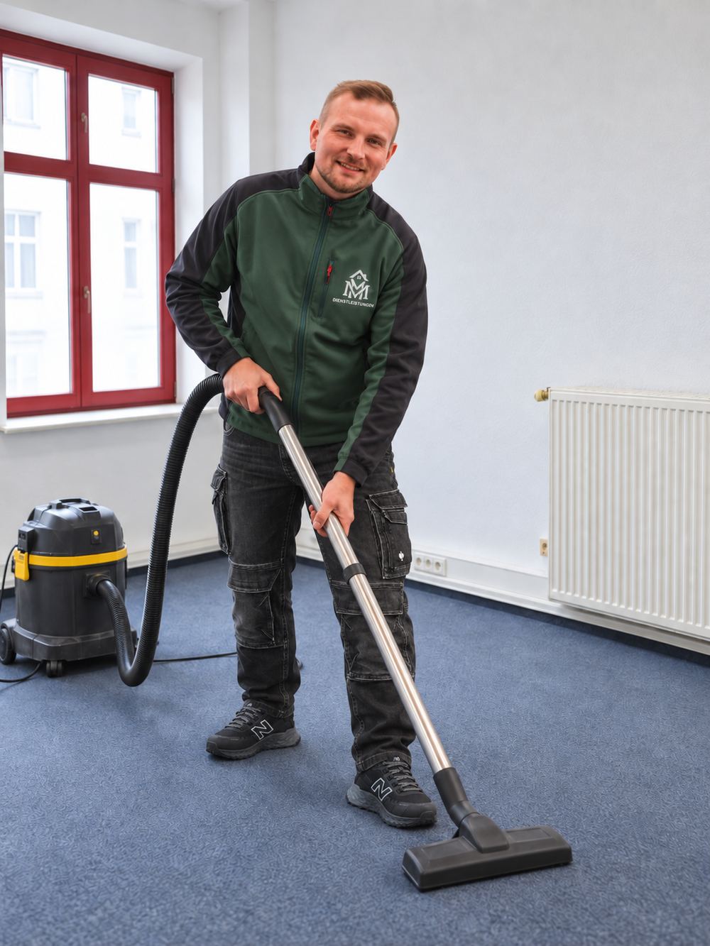 Ein Teammitglied von MM Dienstleistungen saugt einen leeren Raum mit blauem Teppichboden