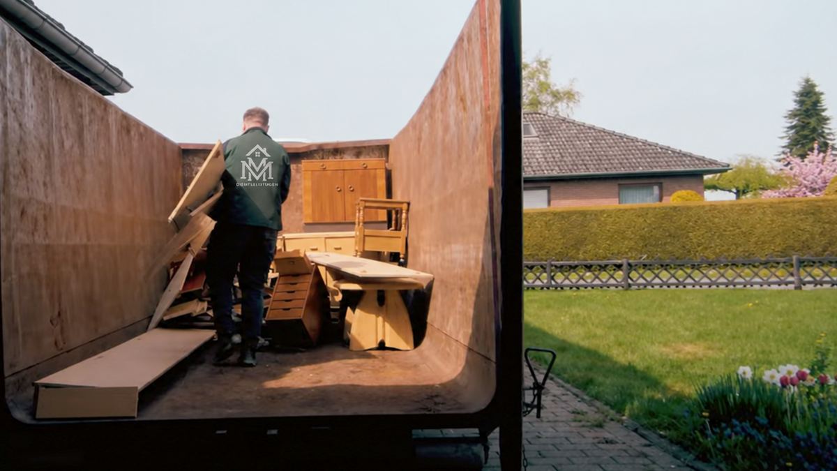Ein Teammitglied von MM Dienstleistungen lädt Holzteile in einen großen Abrollcontainer in einem Wohngebiet