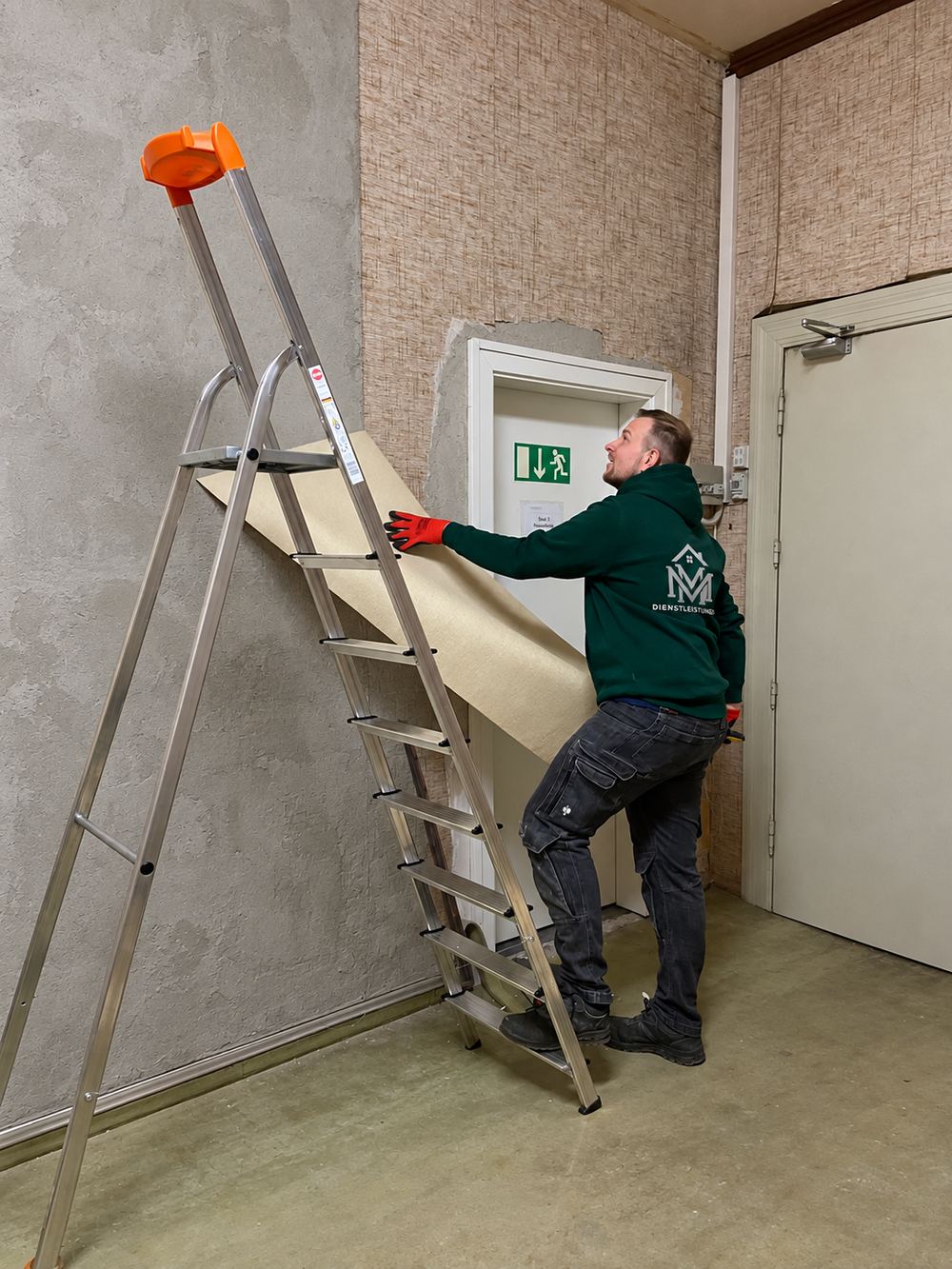 Ein Teammitglied von MM Dienstleistungen steht auf einer Leiter und löst eine Wandverkleidung von der Wand