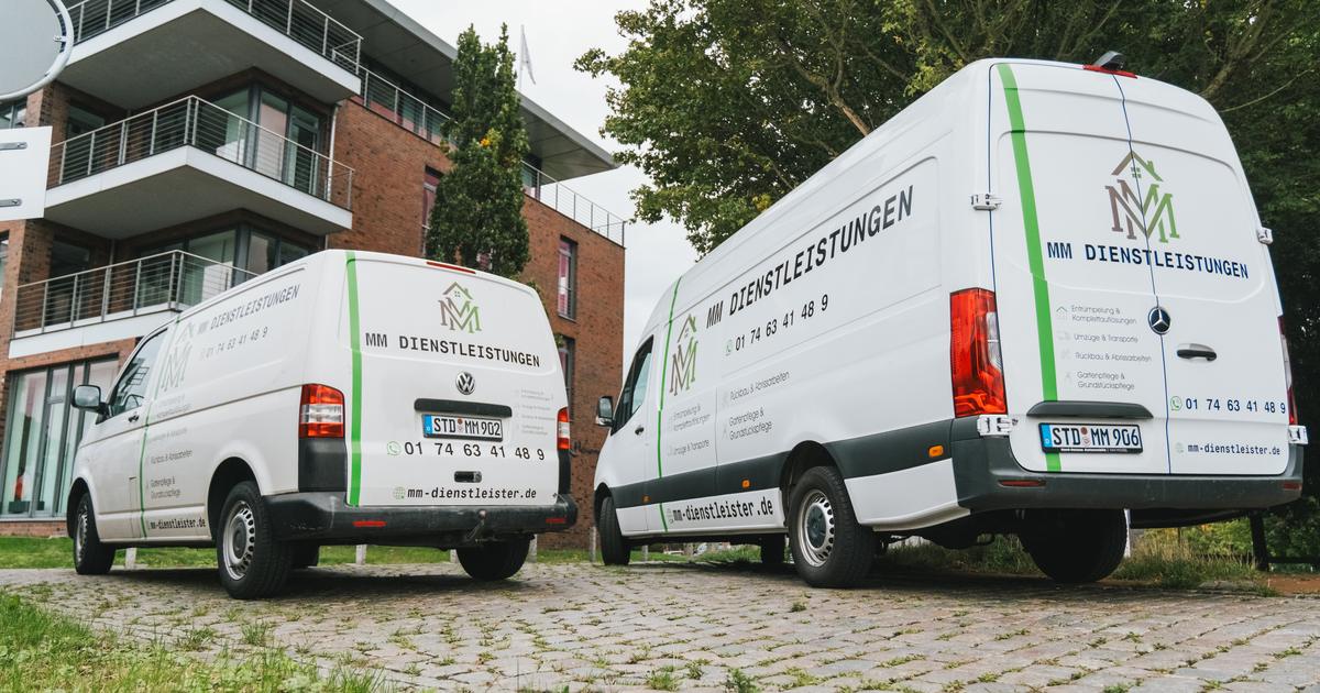 Die beiden beschrifteten Einsatzfahrzeuge von MM Dienstleistungen schräg von hinten auf einem gepflasterten Platz