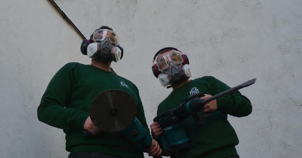 Zwei Teammitglieder von MM Dienstleistungen in Schutzausrüstung mit Atemschutz, Schutzbrille und Gehörschutz, einer mit Trennschleifer, einer mit Stemmhammer