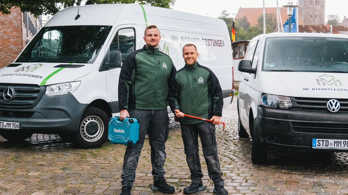 Meik Mroz und Pascal Vagts von MM Dienstleistungen in Arbeitsjacken mit Werkzeug zwischen ihren beiden Einsatzfahrzeugen