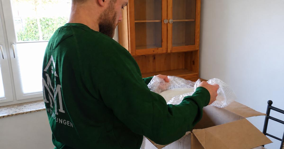 Ein Teammitglied von MM Dienstleistungen verpackt einen Gegenstand sorgfältig in Luftpolsterfolie über einem offenen Umzugskarton