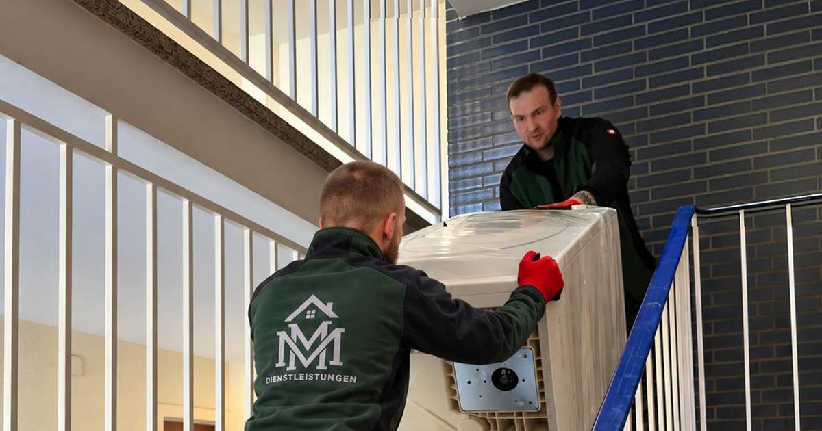 Zwei Teammitglieder von MM Dienstleistungen bringen eine Waschmaschine auf der Sackkarre durch das Treppenhaus nach oben